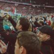 Football fans using smartphones in a crowded stadium, illustrating World Cup ticket and phishing scam risks.