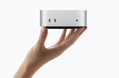 Apple Mac mini with M6 held in a hand, showing the compact desktop's front USB-C ports and headphone jack