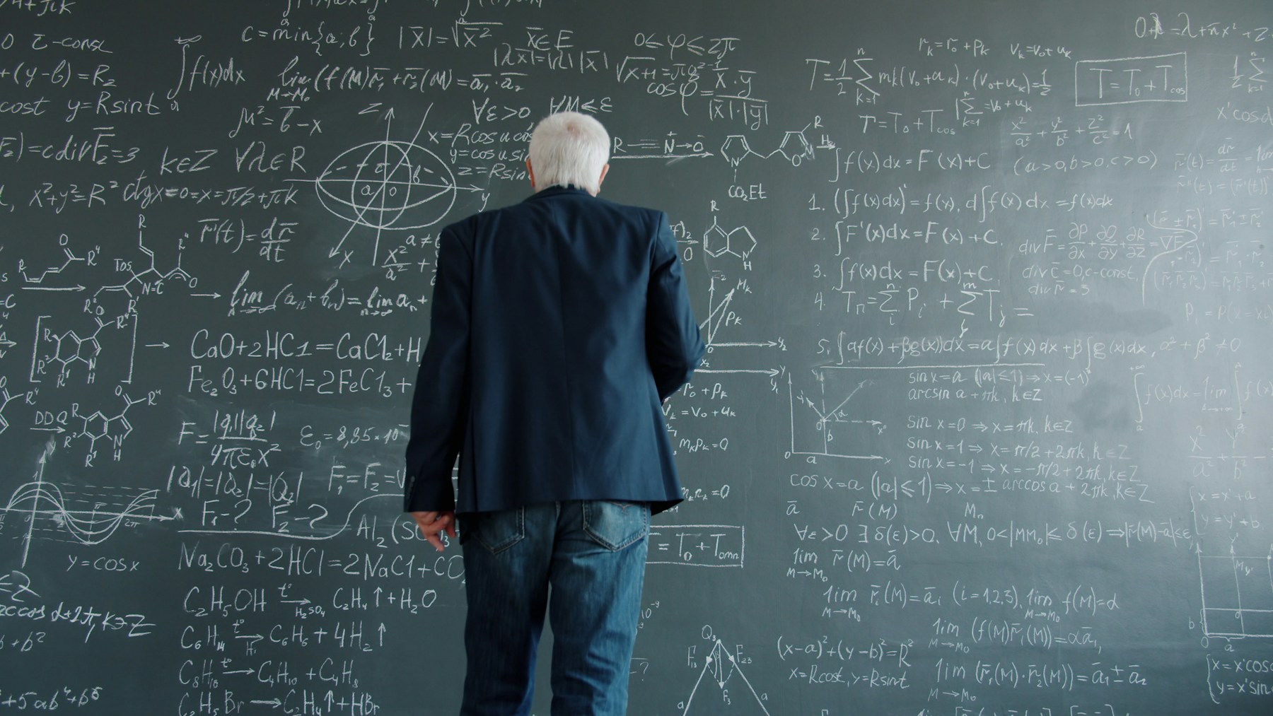 Professor studying a chalkboard covered with mathematical equations